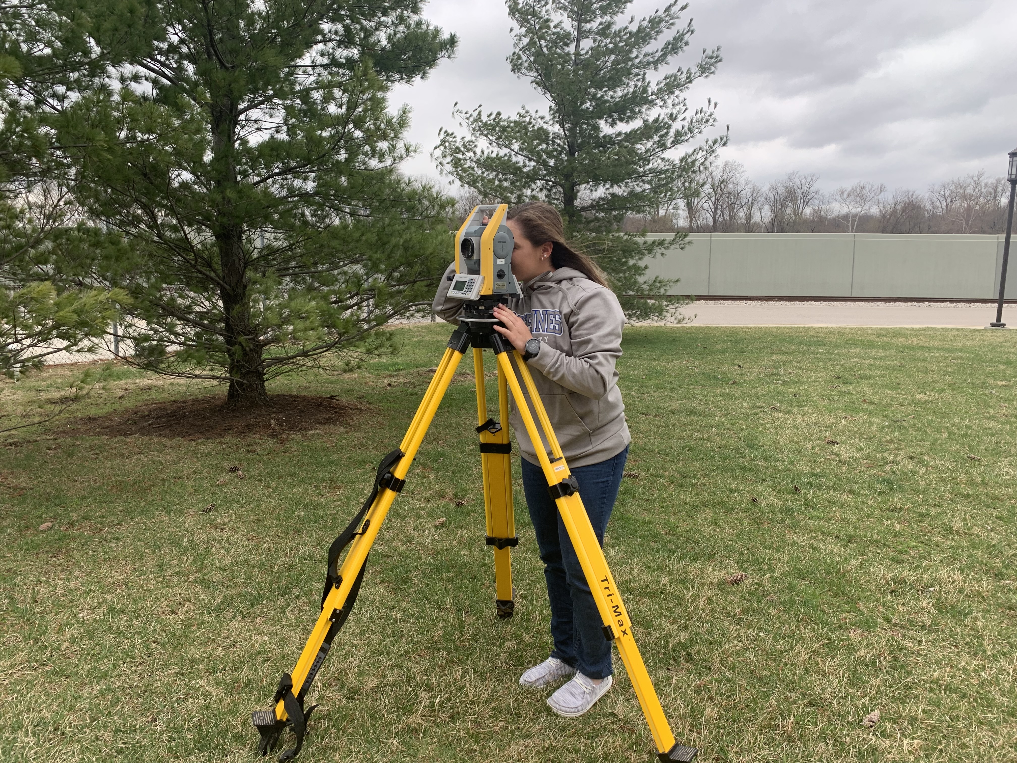 Karissa Gayer operates surveying equipment while she stands near trees