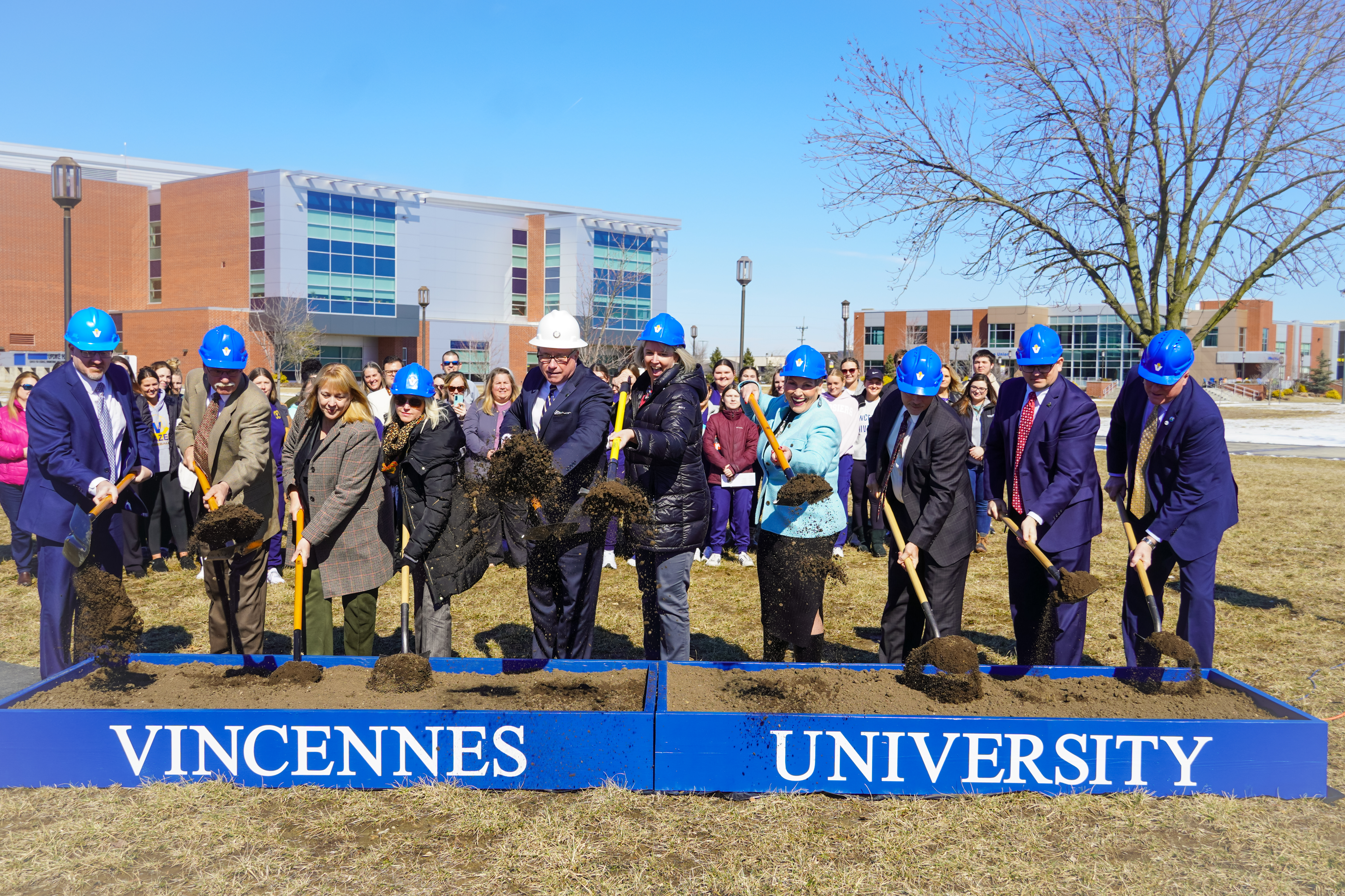 Wearing hard hats and holding shovels, group of VU leaders and community leaders lifts there shovels with dirt into the air.