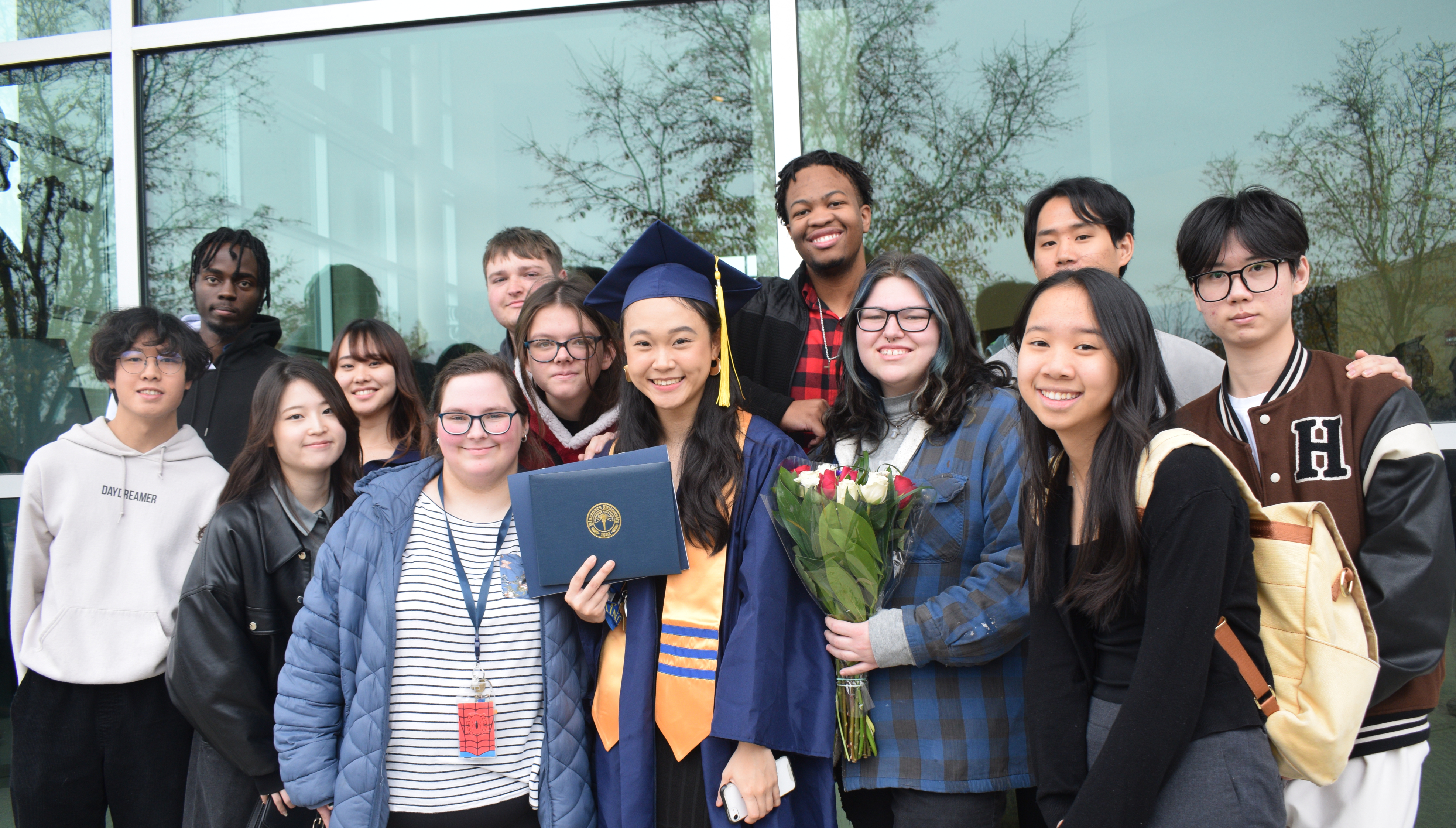 A diverse group of VU students and a VU graduate wearing a cap and gown pose for a group photo.