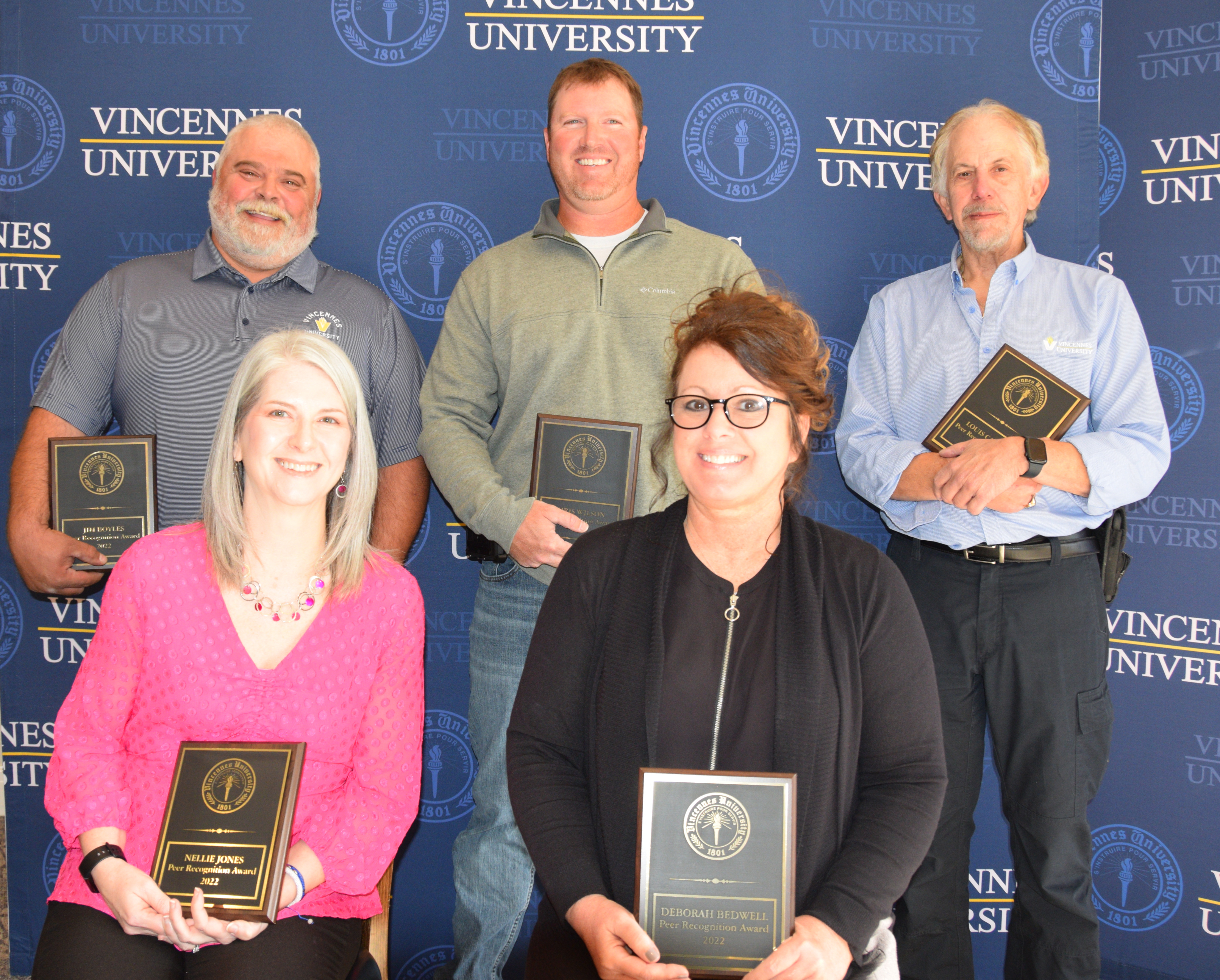 Five 2022 Peer Recognition Award recipients pose together with their awards in front of a VU backdrop
